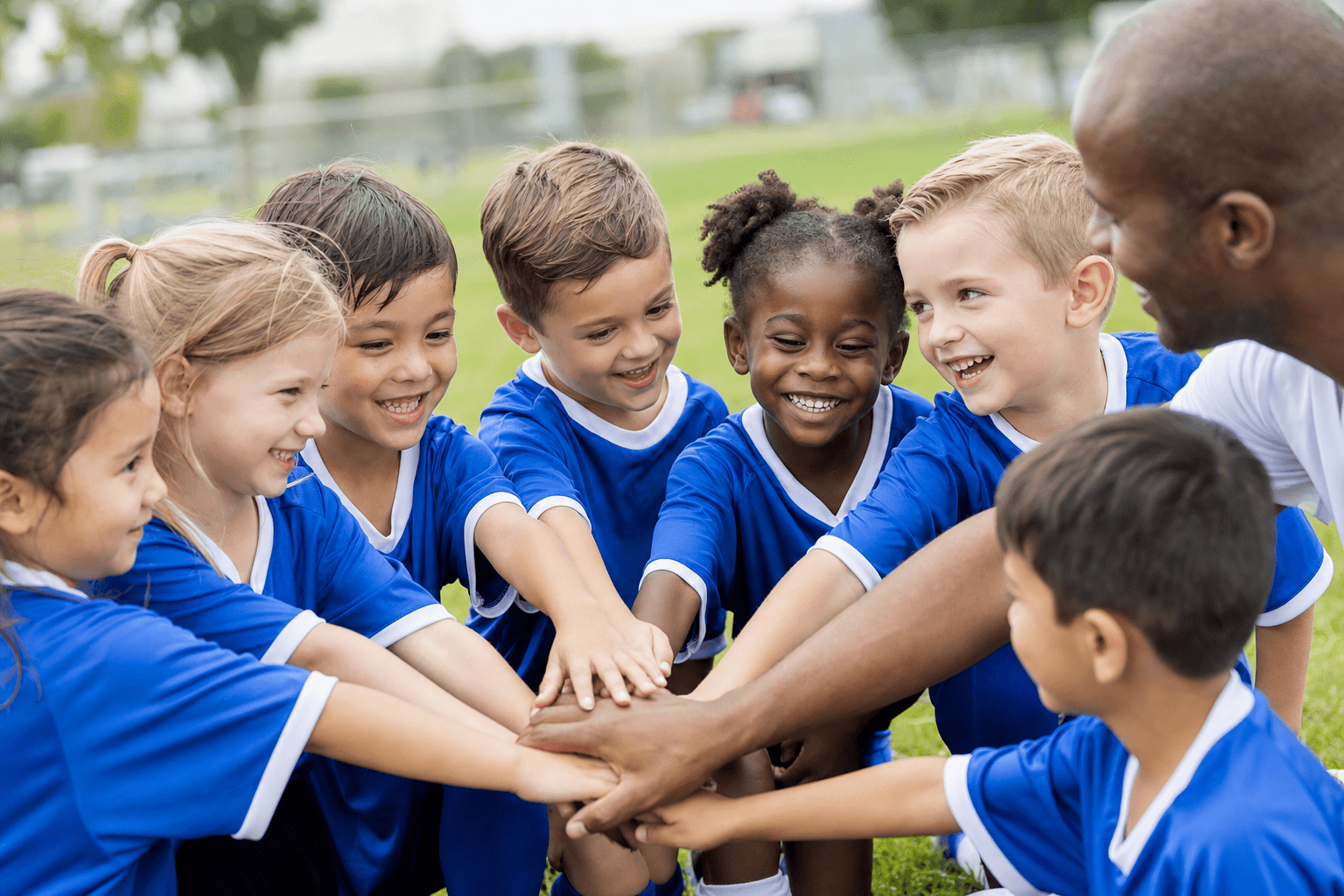 A K–2 youth soccer team huddled together with hands stacked in unity